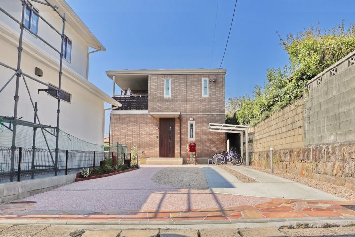 ピンクの乱形石の駐車場　赤いボビポスト　レンガをつかった花壇